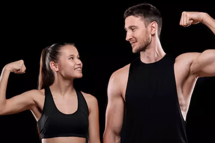 Homme et femme en sportswear noir se regardent en souriant, bras fléchis sur fond noir.